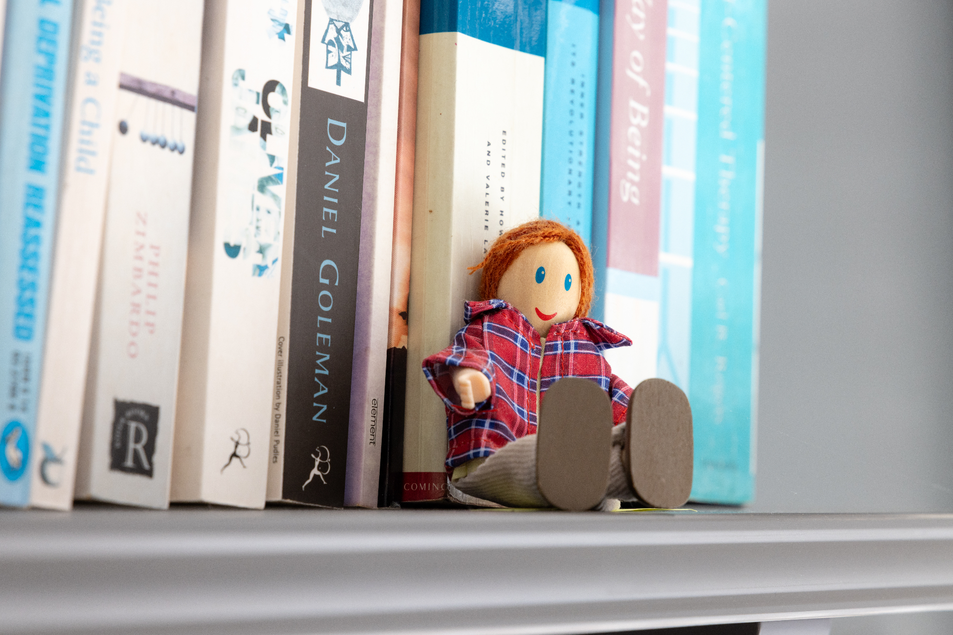 A small wooden doll tucked between psychology books on a shelf in Kate's therapy room
