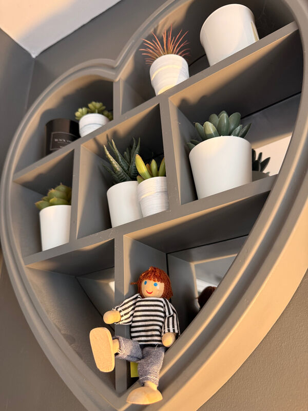 A heart-shaped wall shelf with succulents and a small wooden doll in Kate Ramsay's therapy room