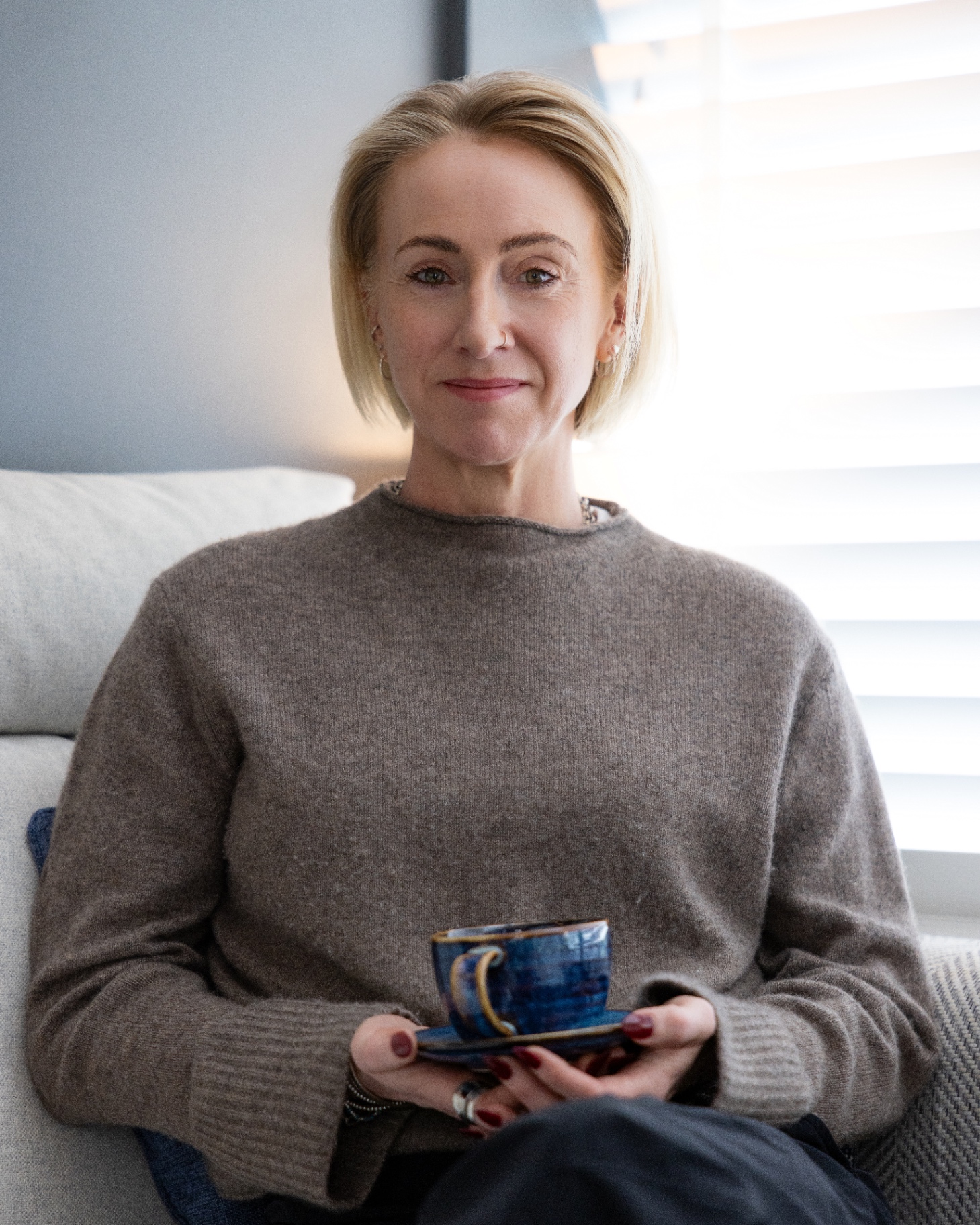 Kate Ramsay holding a handmade cup, seated on a sofa
