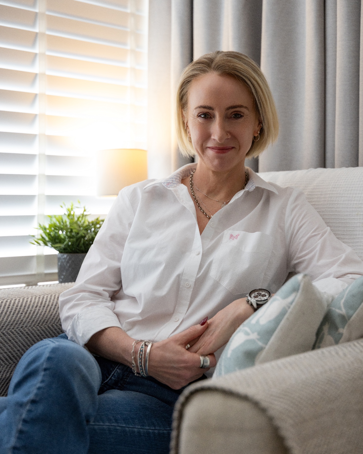 Kate Ramsay seated on a sofa in a softly lit room, white shirt